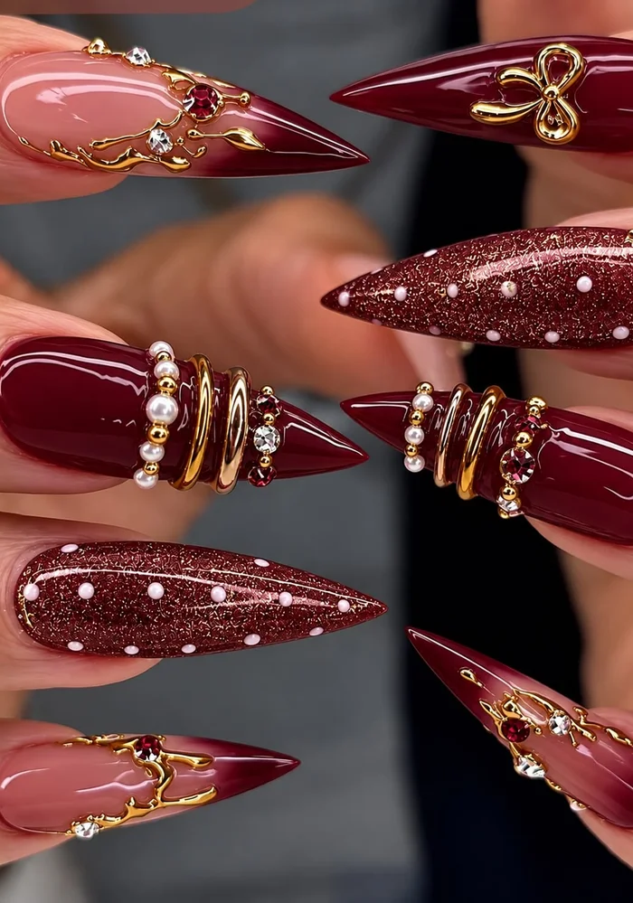 Burgundy stiletto nail set with gold charms, pearls and crystals